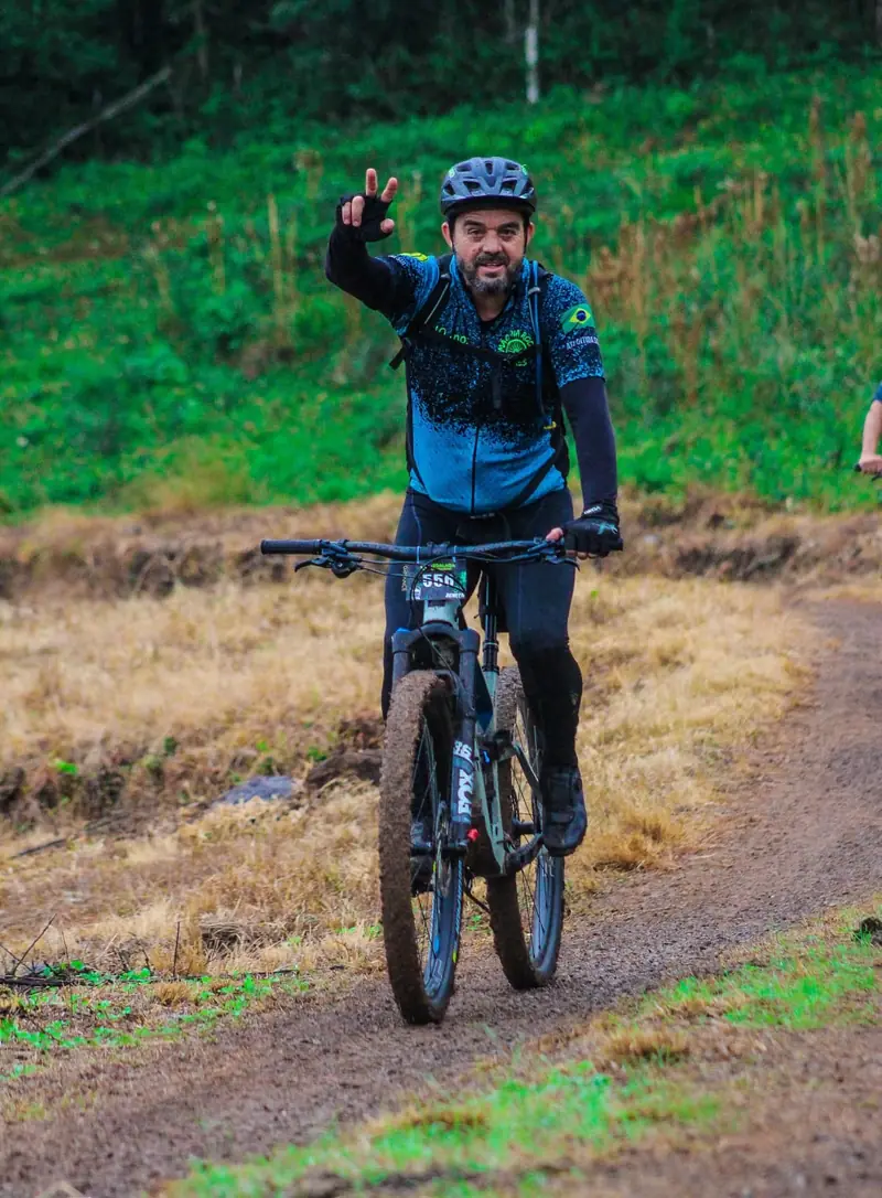 Ciclista acenando com a mão enquanto pedala em trilha de terra