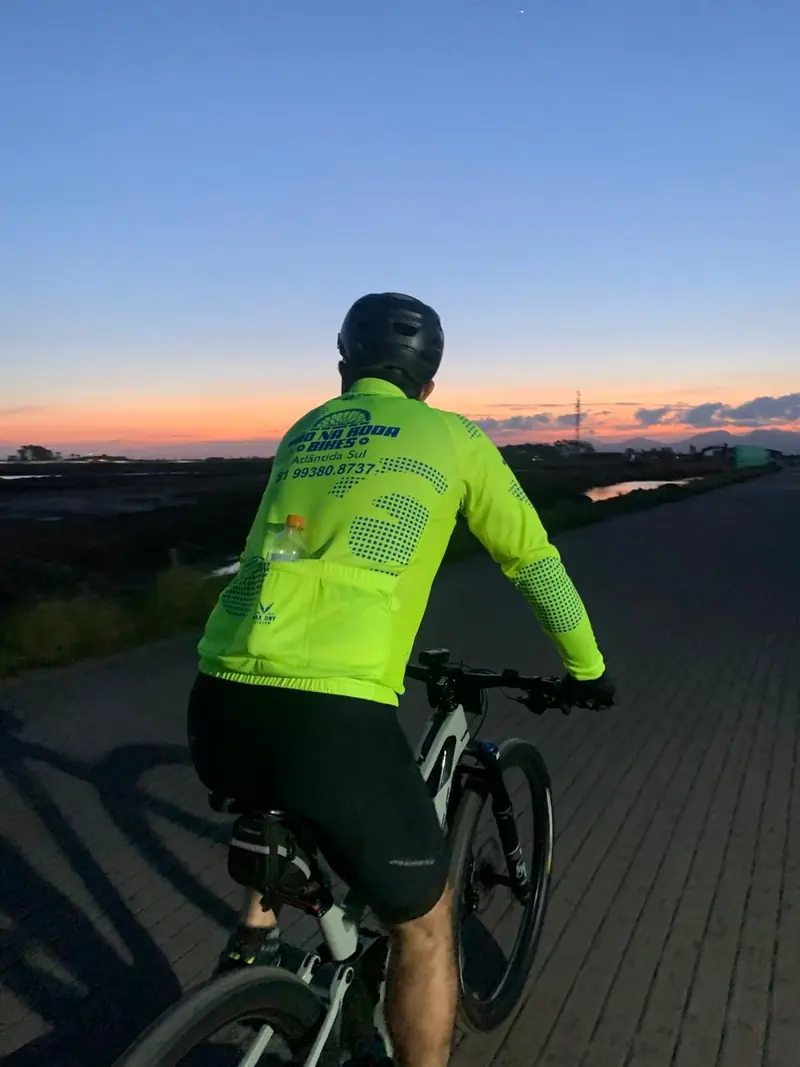 Ciclista com blusa refletiva pedalando com o céu alaranjado do fim do dia ao fundo