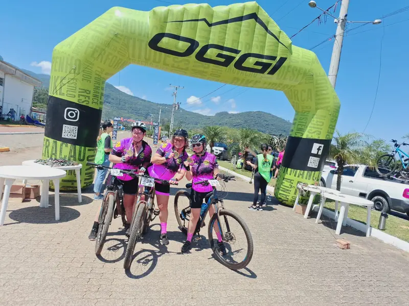 Três ciclistas posam com as bikes sob o arco inflável da Oggi na largada do passeio