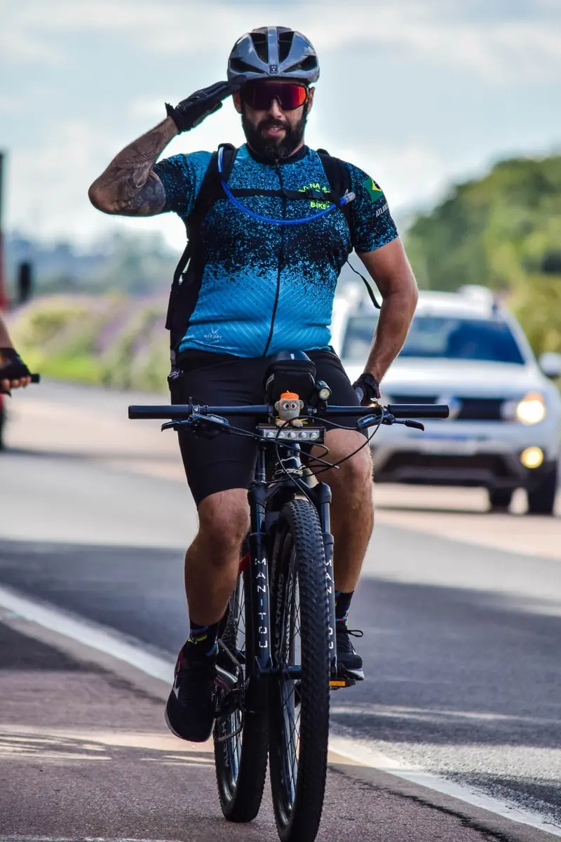 Ciclista fazendo continência para a câmera enquanto pedala na estrada