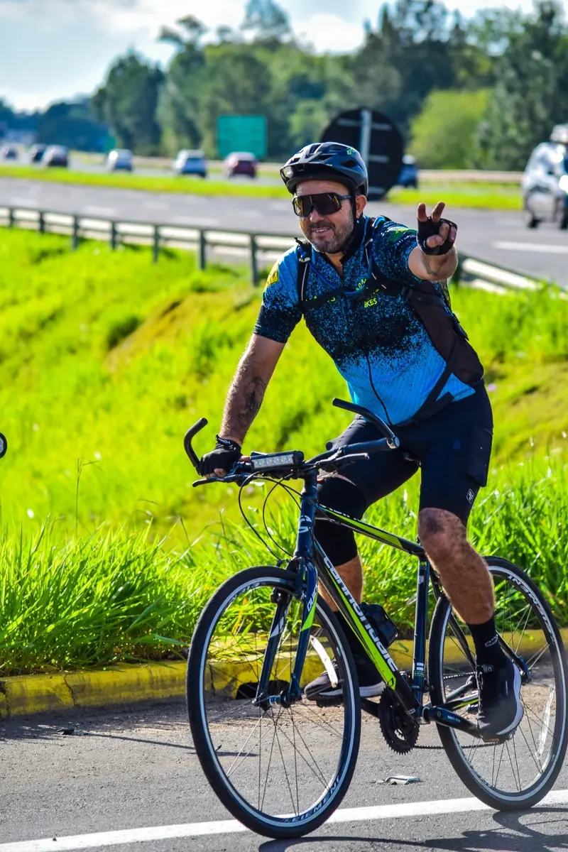 Ciclista acenando com o sinal de paz enquanto pedala na beira de uma rodovia