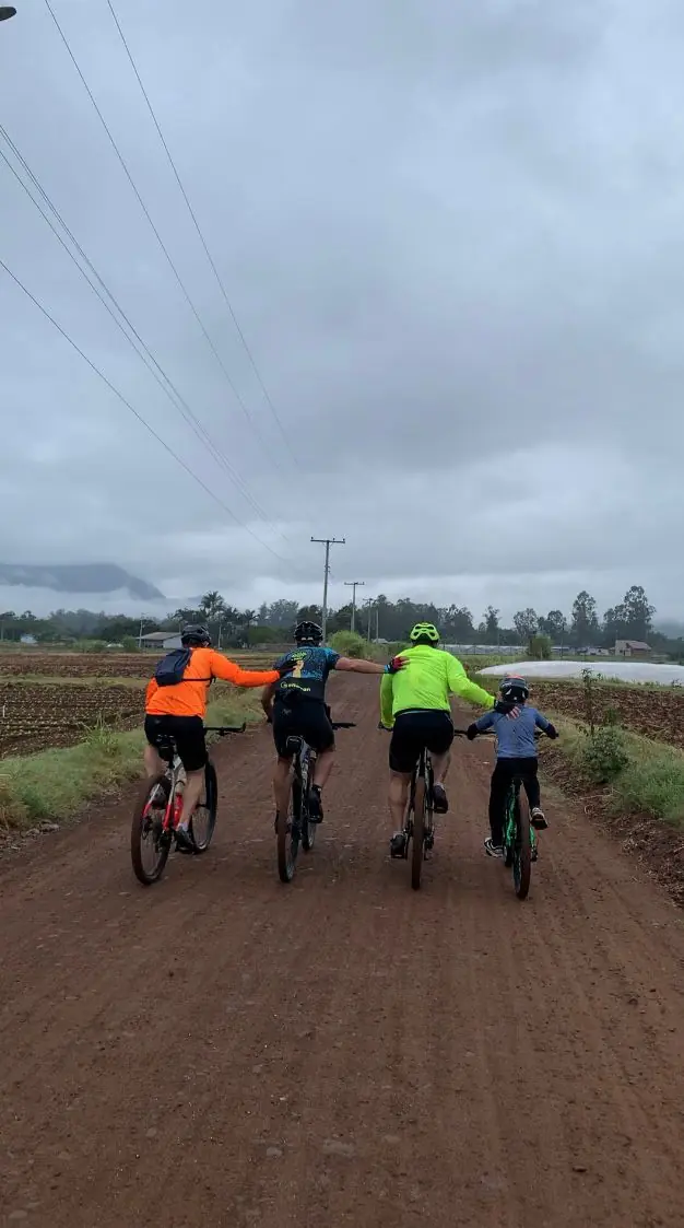 Grupo de ciclistas, visto de costas, pedalando em estrada de terra em dia nublado