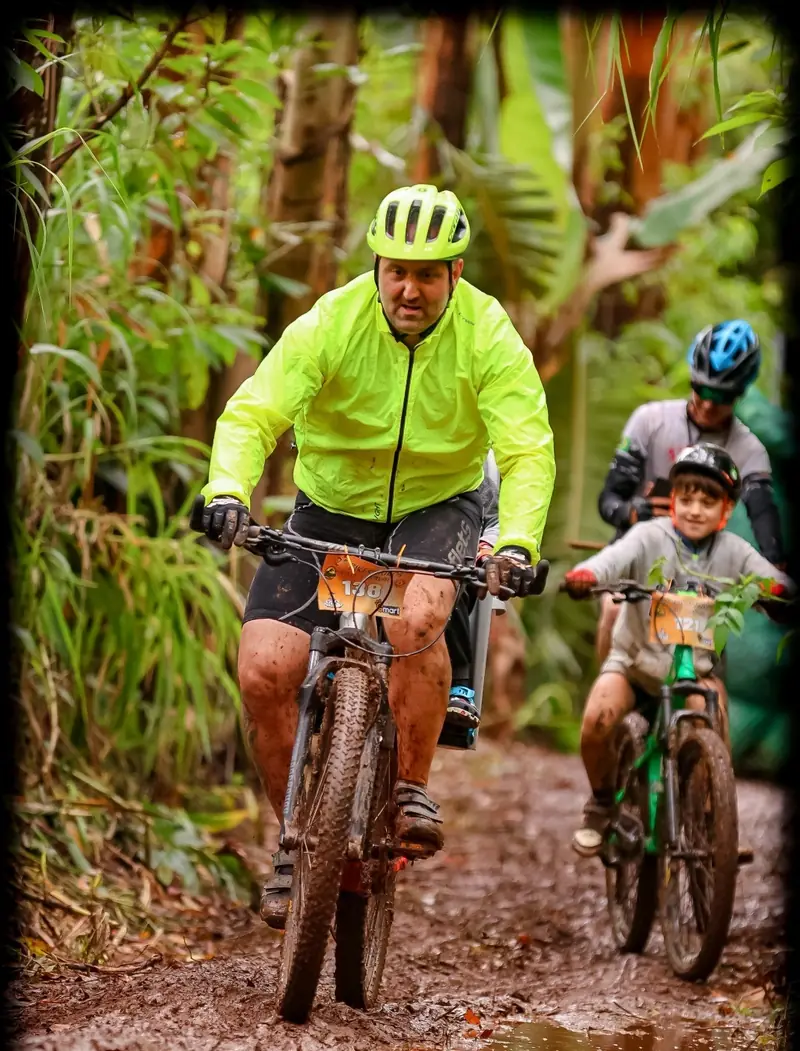 Adulto e criança pedalando juntos em trilha cercada de vegetação