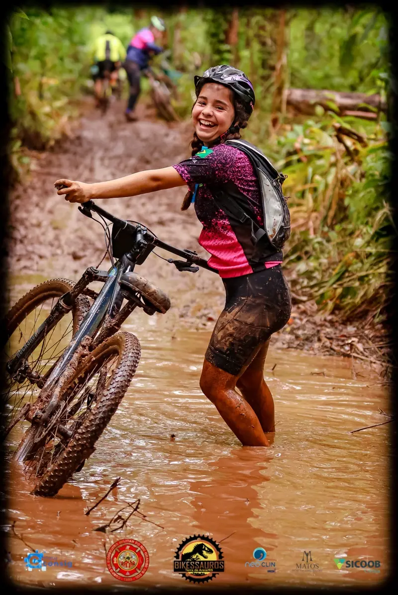 Ciclista sorrindo ao atravessar uma poça de lama com a bike na trilha
