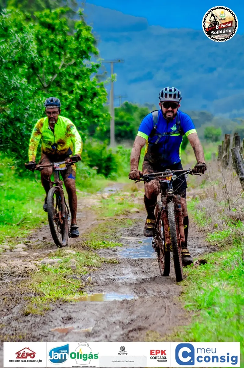 Dois ciclistas pedalando em trilha de terra com lama, em meio ao verde