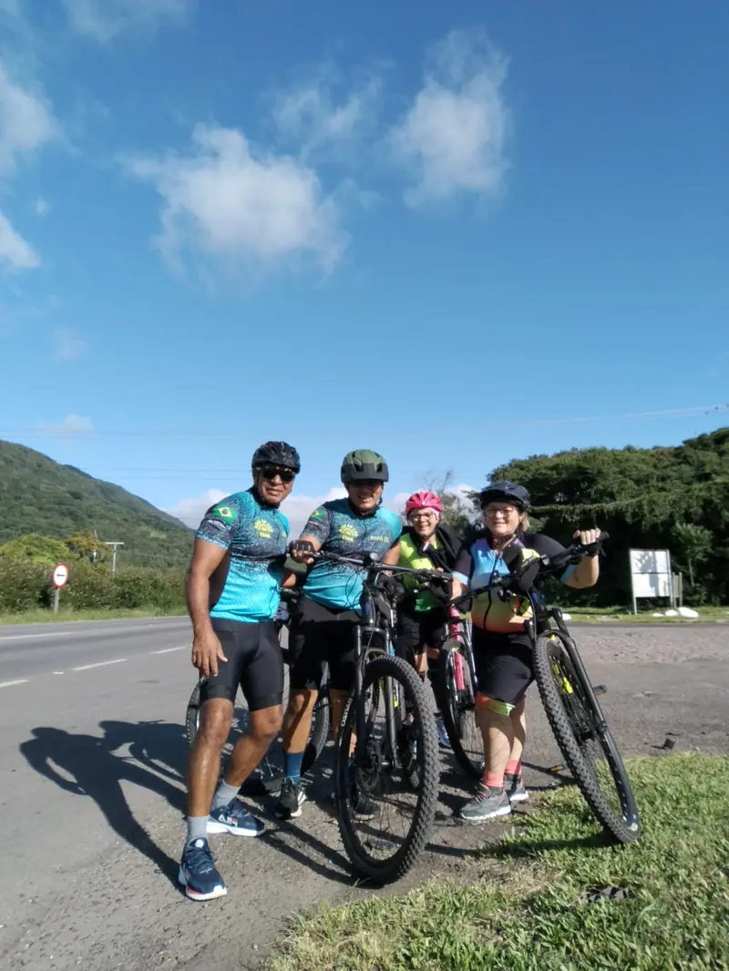 Grupo de ciclistas parado com as bikes no acostamento, com morros ao fundo