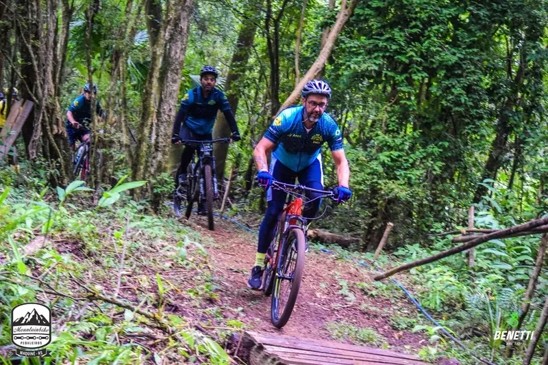 Ciclista descendo uma trilha na mata, sobre uma ponte de madeira