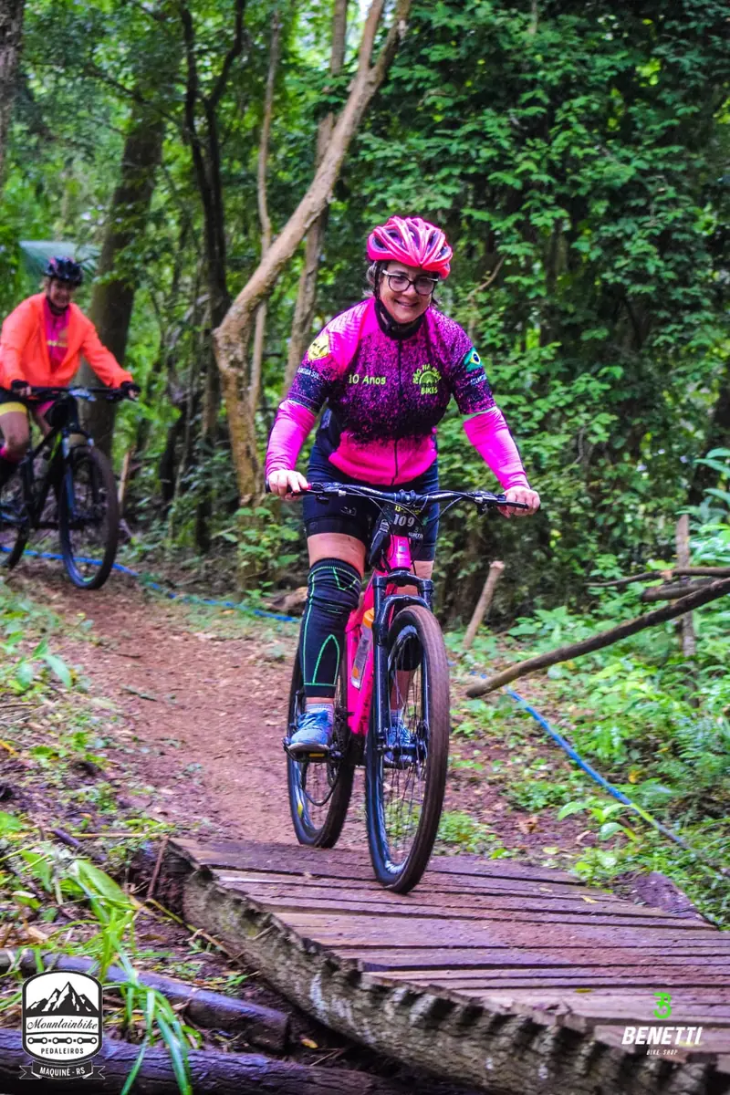 Ciclista de uniforme rosa pedalando em trilha de terra na mata