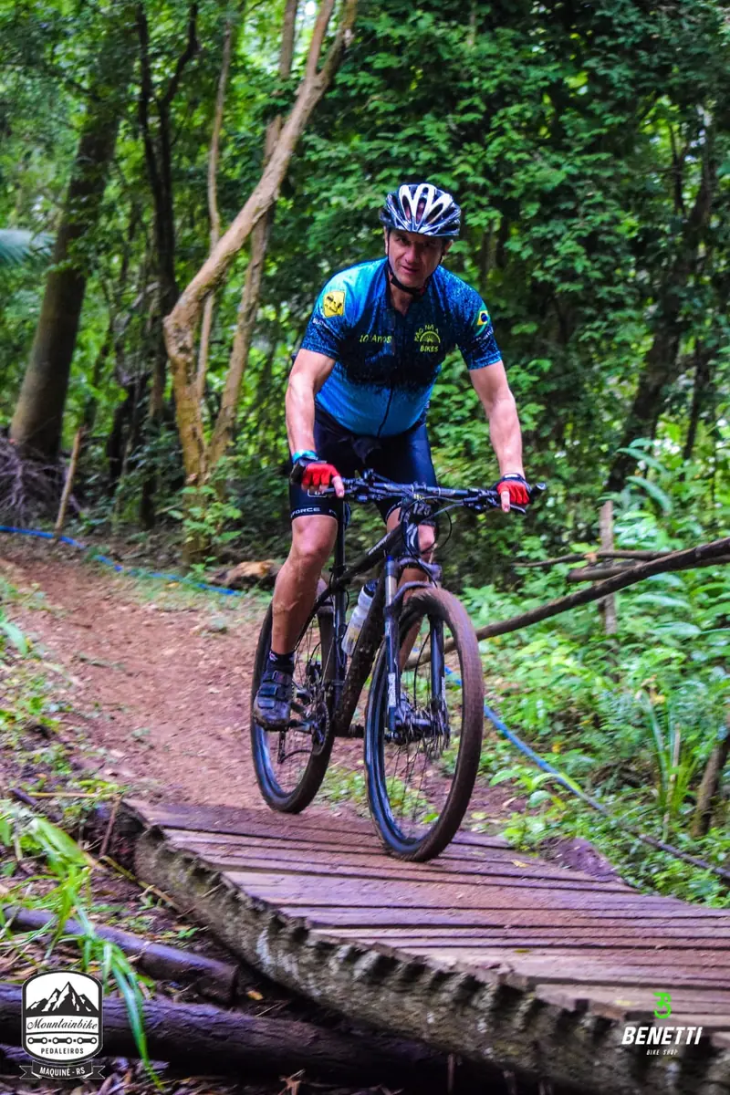 Ciclista de camisa azul pedalando em trilha de terra, sobre pontes de madeira